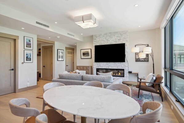A modern living room with a fireplace, a flat-screen TV, and a dining area with a round table and chairs.