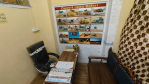 A room with a wooden table, a black office chair, a wooden bench, and a bulletin board with a 'Desert Jeep Safari' poster.