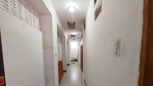 A long, narrow hallway with white walls and a tiled floor. There are doors on both sides, and a vent is visible on the ceiling.