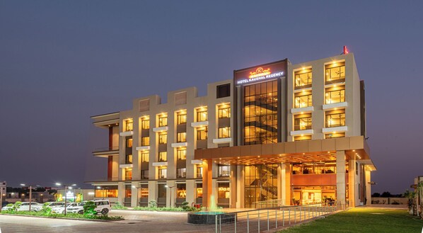 Un hotel de varios pisos con fachada moderna, ventanas iluminadas y una entrada visible con escaleras.