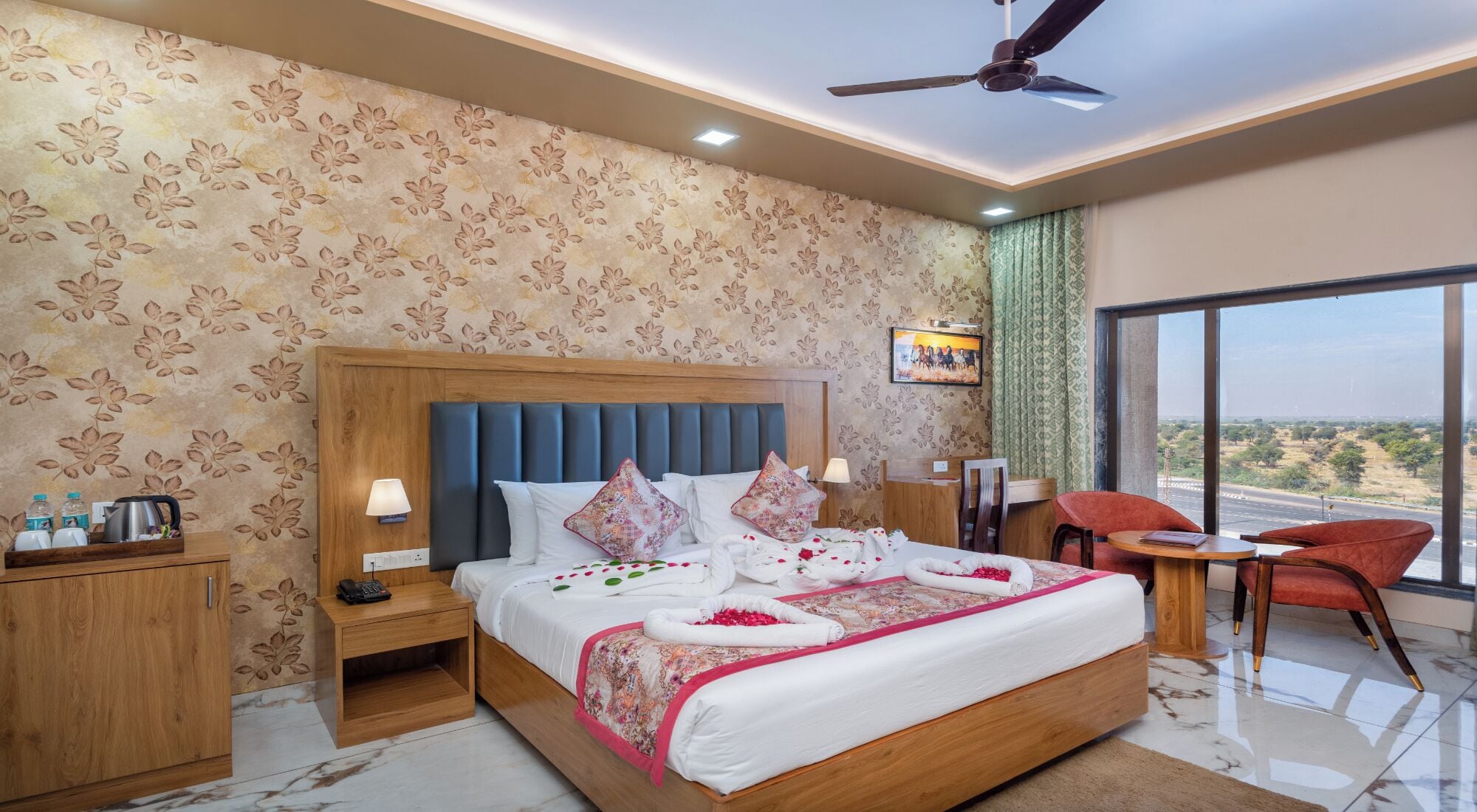 A hotel room with a large bed, a desk, a chair, and a view of the outdoors.