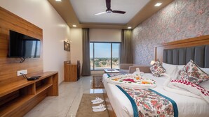 A hotel room with a bed, a TV, a desk, and a view of the outdoors. - Hotel Kaushal Regency (Refinery Road Pachpadra) (Pachpadra)
