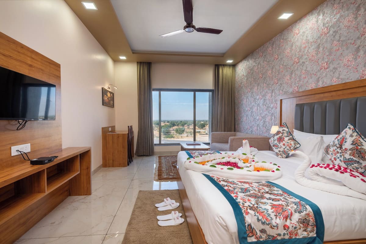 A hotel room with a bed, a TV, a desk, and a view of the outdoors.