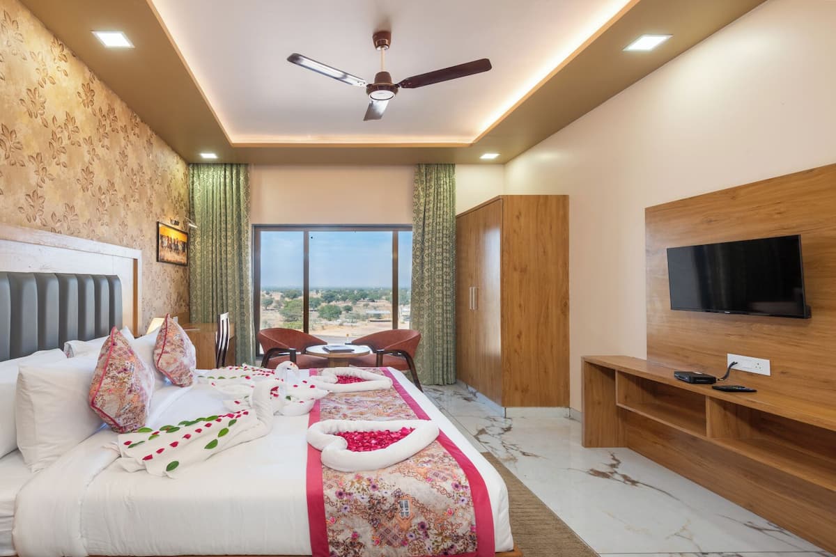 A hotel room with a large bed, a ceiling fan, a TV, and a view of the outdoors.