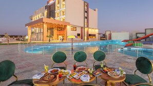 A hotel with a pool area, outdoor dining with multiple tables and chairs, and a water slide. - Hotel Kaushal Regency (Refinery Road Pachpadra) (Pachpadra)