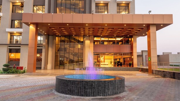 A modern building with a central courtyard featuring a circular water fountain. - Hotel Kaushal Regency (Refinery Road Pachpadra) (Pachpadra)