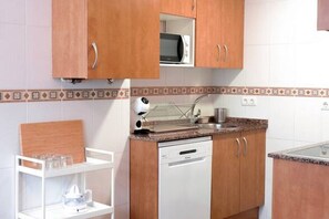 A compact kitchen with wooden cabinets, a microwave, a dishwasher, and a white countertop. - 11A02 Casa RTPG  6p (Castrillon)