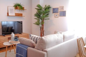 A living room with a sofa, a television, a small table with a vase, and a plant. - 11A02 Casa RTPG  6p (Castrillon)