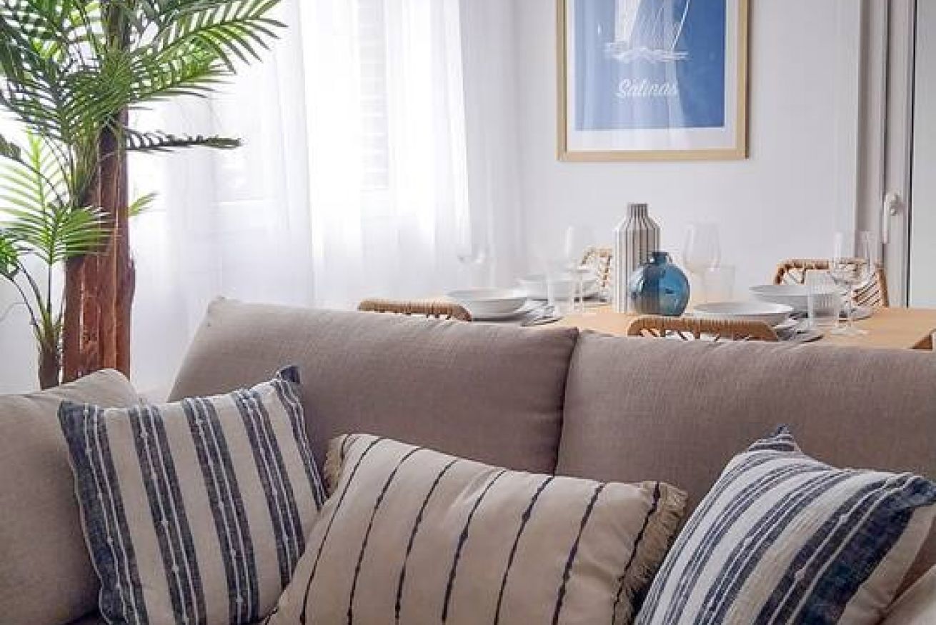 A living room with a sofa, striped cushions, a dining table set with plates, glasses, and a vase.
