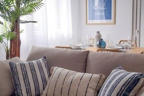 A living room with a sofa, striped cushions, a dining table set with plates, glasses, and a vase. - 11A02 Casa RTPG  6p (Castrillon)