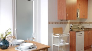 A dining area with a wooden table set for two, a white cabinet, and a kitchen area with a dishwasher. - 11A02 Casa RTPG  6p (Castrillon)