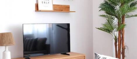 A modern living room with a flat-screen TV on a wooden stand, a lamp, a sofa, and a potted plant.