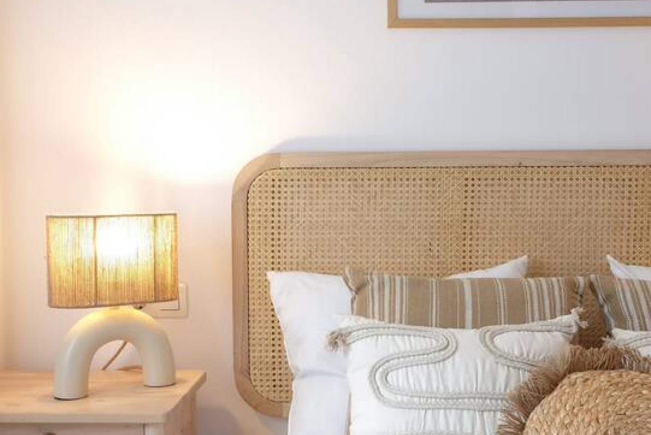Un lit avec une tête de lit en osier, une lampe de chevet et plusieurs oreillers.