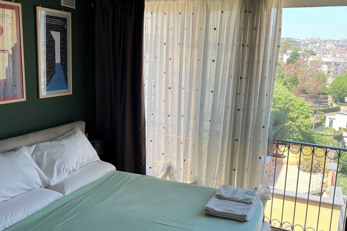 A bedroom with a bed, a window with curtains, and a balcony with a railing.