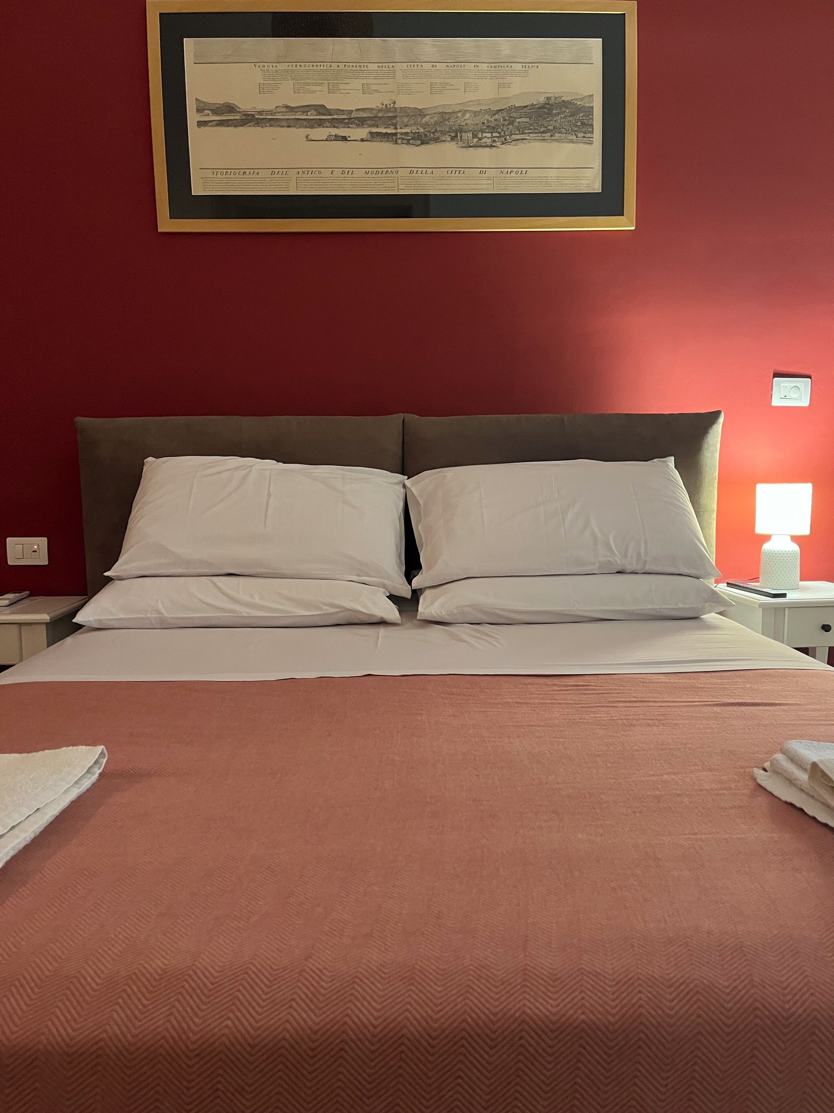 A neatly made bed with white linens and a brown headboard in a room with red walls.