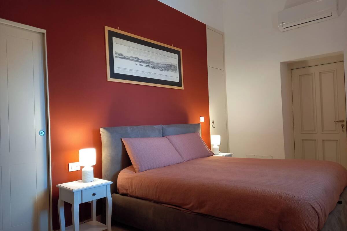 A bedroom with a bed, nightstands, a framed picture on the wall, and a door.