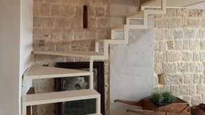 Un interior rústico con paredes de piedra vista, un carromato de madera y una escalera que sube a una zona de entrepiso.