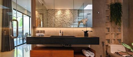 Un baño moderno con un espejo grande, revestimiento de pared de piedra y una sauna integrada.