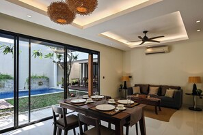 A modern living room with a dining area, a ceiling fan, and a view of a swimming pool. - The Cabana Villa (Seminyak)