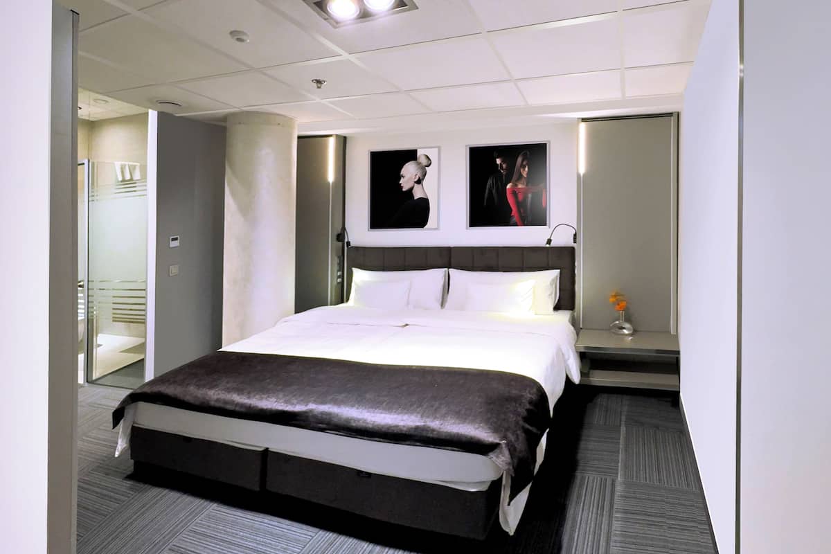 A modern hotel room with a large bed, a nightstand, and a mirror.