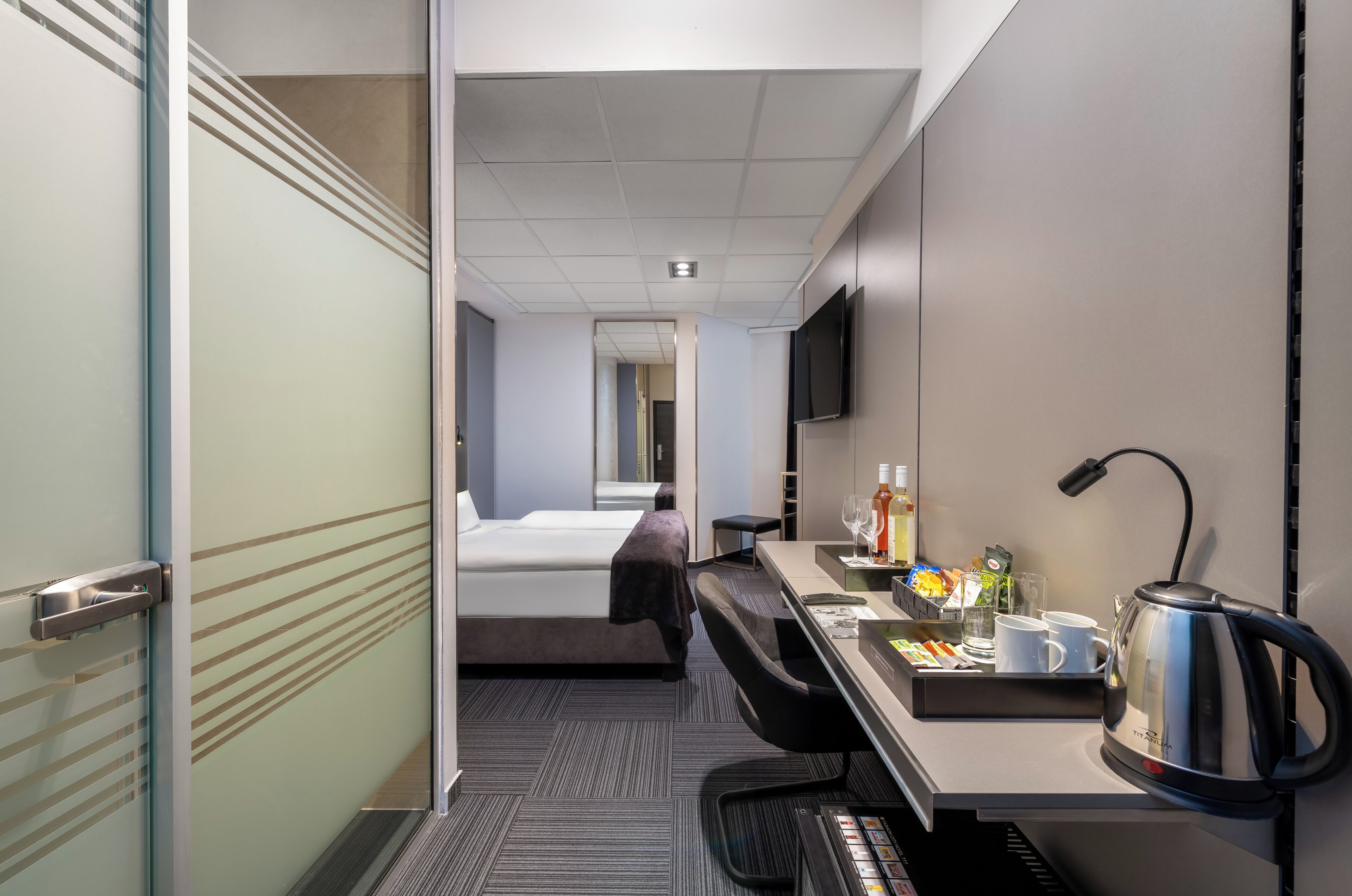A hotel room with a bed, desk, coffee maker, and a TV mounted on the wall.