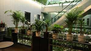Un espacio interior moderno con varios niveles, con plantas en macetas sobre las barandillas y una escalera central.