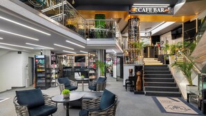 Un vestíbulo de hotel de varios niveles con un café-bar, mostrador de recepción y una escalera.