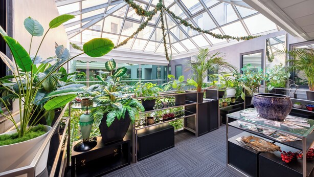 Un amplio atrio con techo de vidrio, grandes macetas con plantas y una mesa de exhibición central.