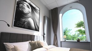 Una habitación de hotel moderna con una cama grande, un ventanal con vistas a zonas verdes y un cartel en la pared.