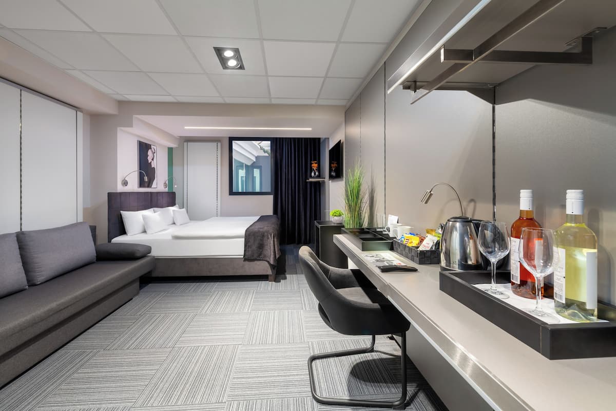 A modern hotel room with a sofa, bed, desk, and a large mirror.