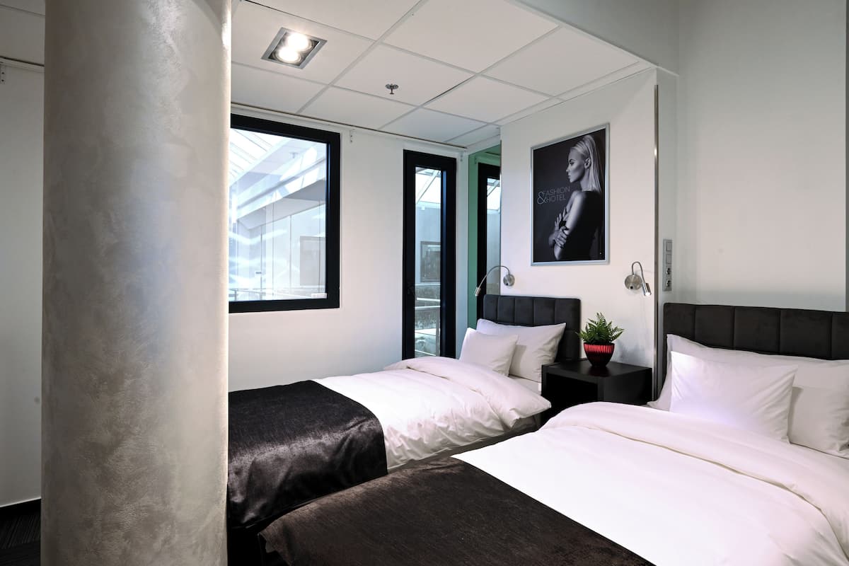 A hotel room with two beds, a large window, a ceiling light, and a wall-mounted artwork.