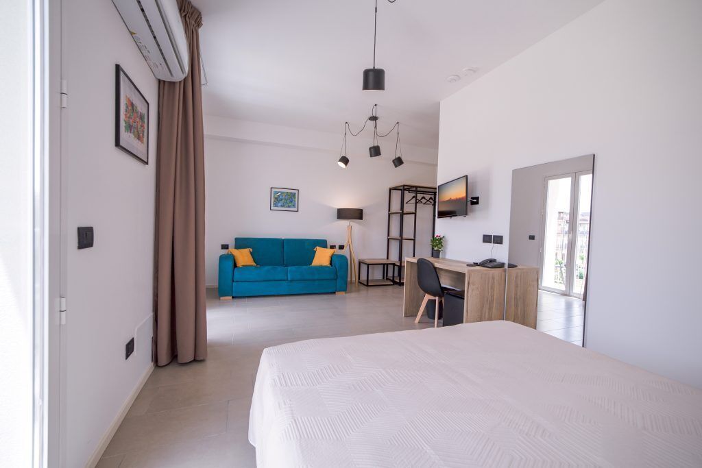 A modern hotel room with a large bed, a desk, a blue sofa, and a TV.