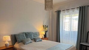 A bedroom with a large bed, two bedside tables with lamps, a chair, and a view of the outdoors through sheer curtains. - Sun And Ocean House With 2 Bathrooms (Alcobaça)