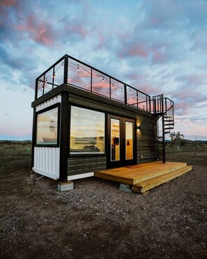 Eine moderne, zweistöckige Holzhütte mit großen Fenstern, einer Holzdiele und einer Wendeltreppe.