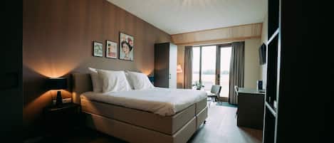 A modern hotel room with a large bed, bedside tables, a desk, and a view of the outdoors.