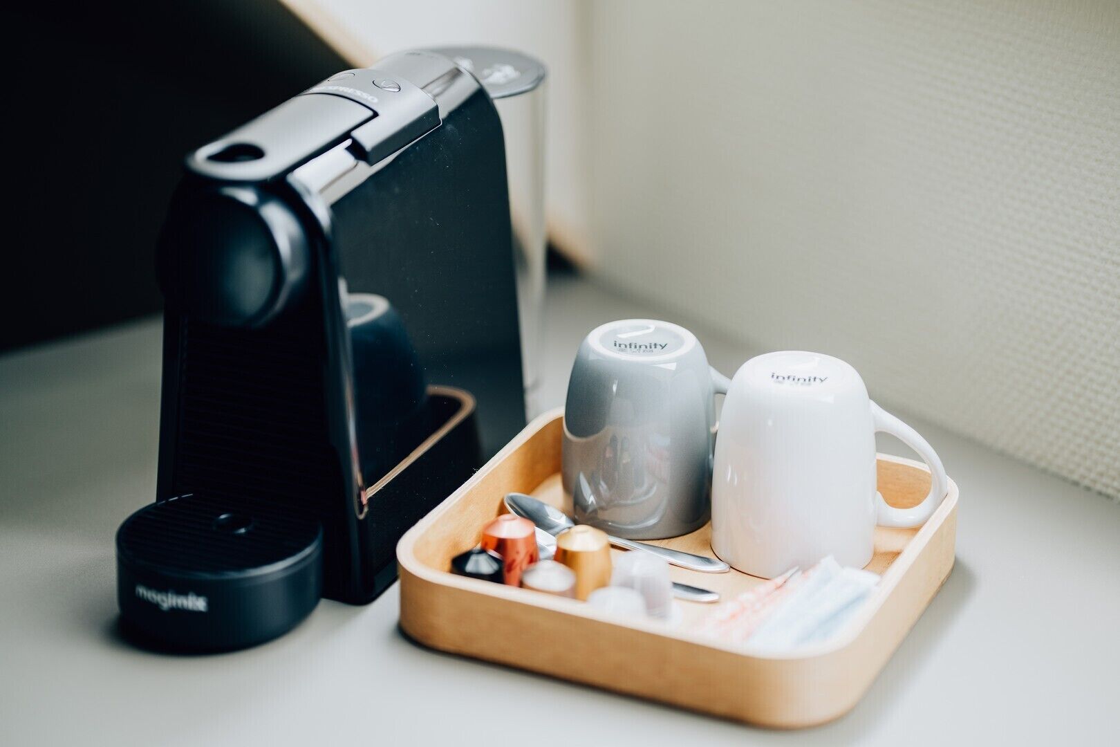 Una cafetera, dos tazas y una bandeja con cubiertos sobre una mesa.