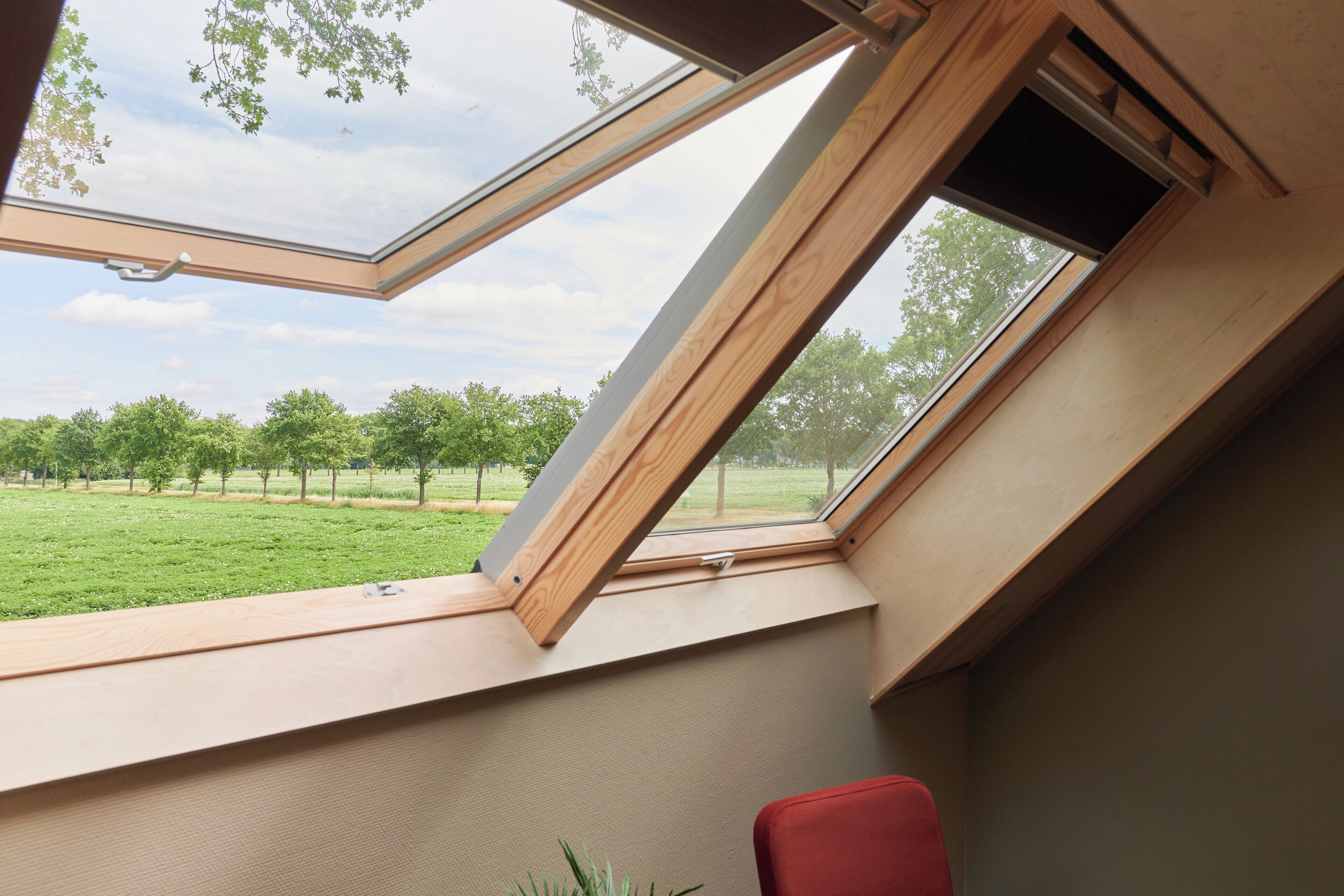 A room with a skylight, a red chair, and a view of a green field with trees.