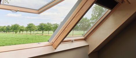 Una habitación con tragaluz, una silla roja y vista a un campo verde con árboles.