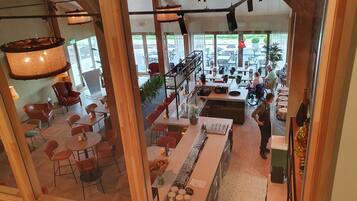 A modern restaurant with wooden beams, a bar area, and outdoor seating visible through large windows.