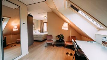Un dormitorio moderno y bien iluminado en el ático, con techo inclinado, una cama, dos sillones, una mesa y una planta en maceta.
