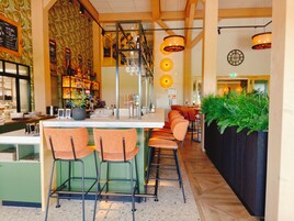 Una zona de bar con mostrador, taburetes y una planta en maceta.