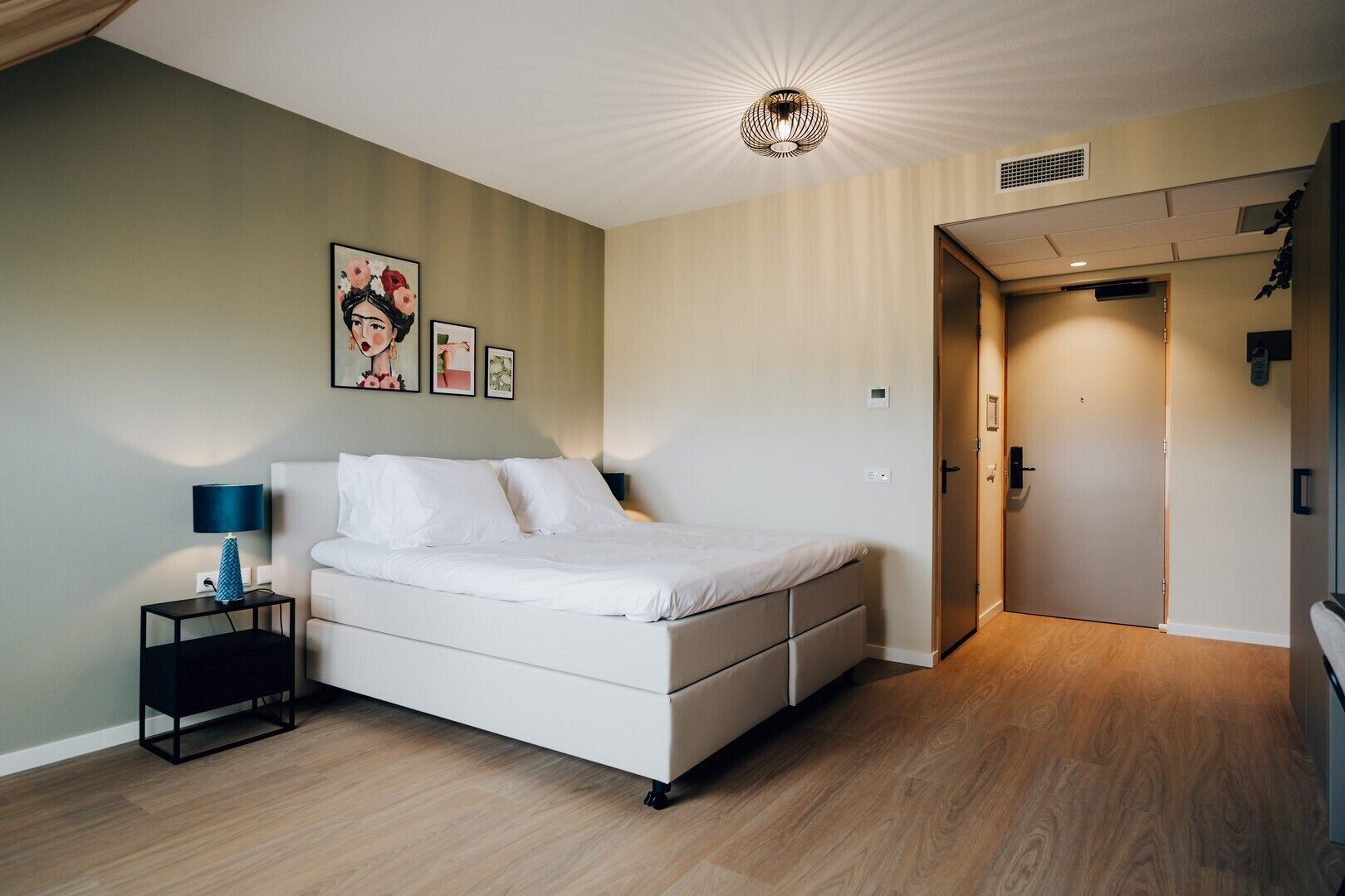 Un dormitorio con cama, mesita de noche, lámpara y puerta que da a otra habitación.
