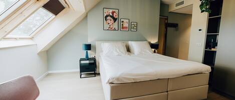 A modern bedroom with a large bed, a desk, and a skylight.