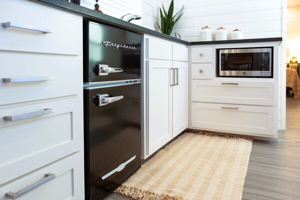 Een moderne keuken met witte kasten, een roestvrijstalen koelkast, een magnetron en een klein plantje op het aanrecht.