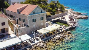 A stone building with a red-tiled roof, outdoor seating, and a view of the sea. - Vila Fenč (Primosten)