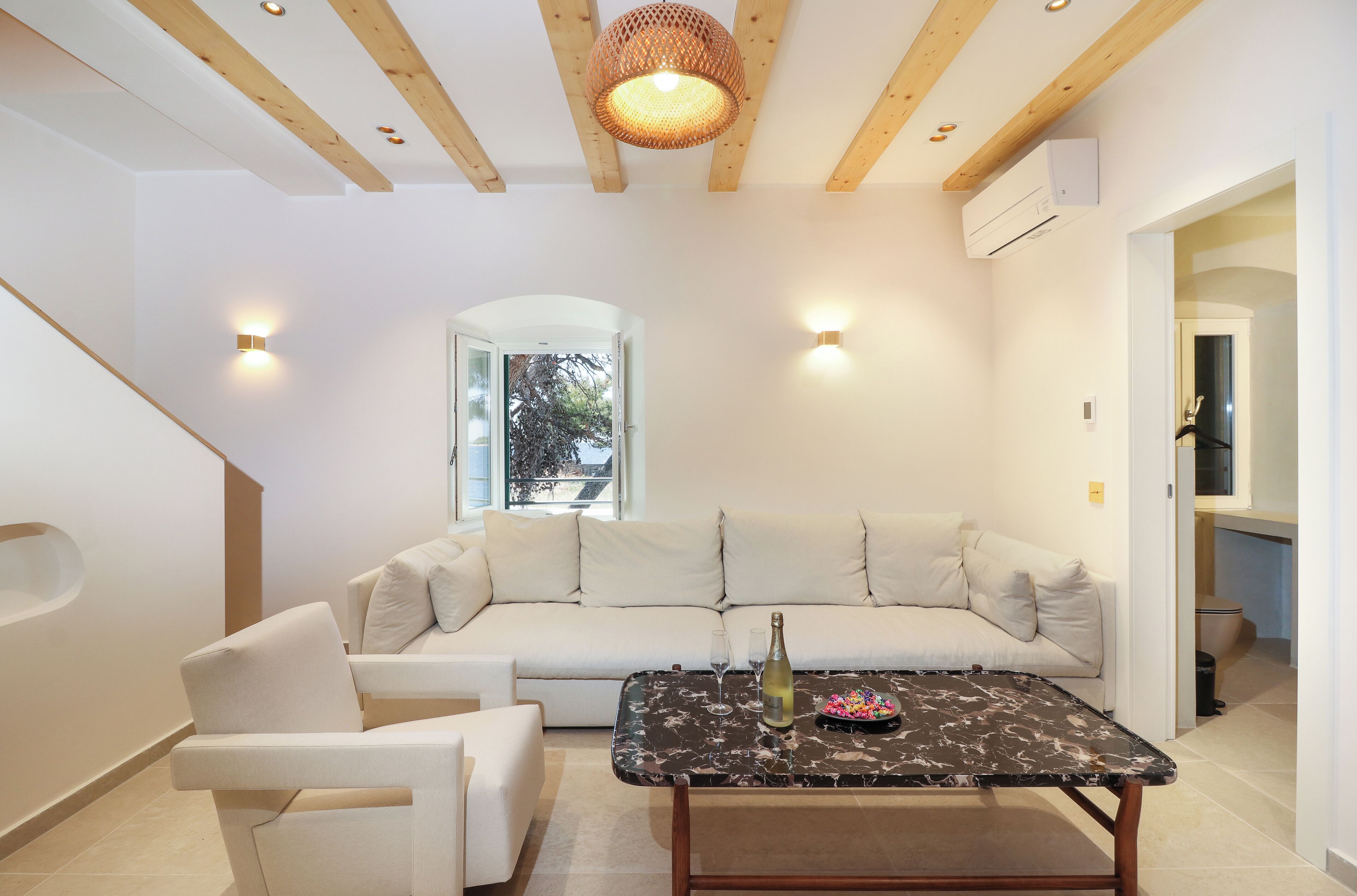 Un salon moderne avec un canapé, une table basse et un fauteuil. On peut voir une bouteille et des verres sur la table.