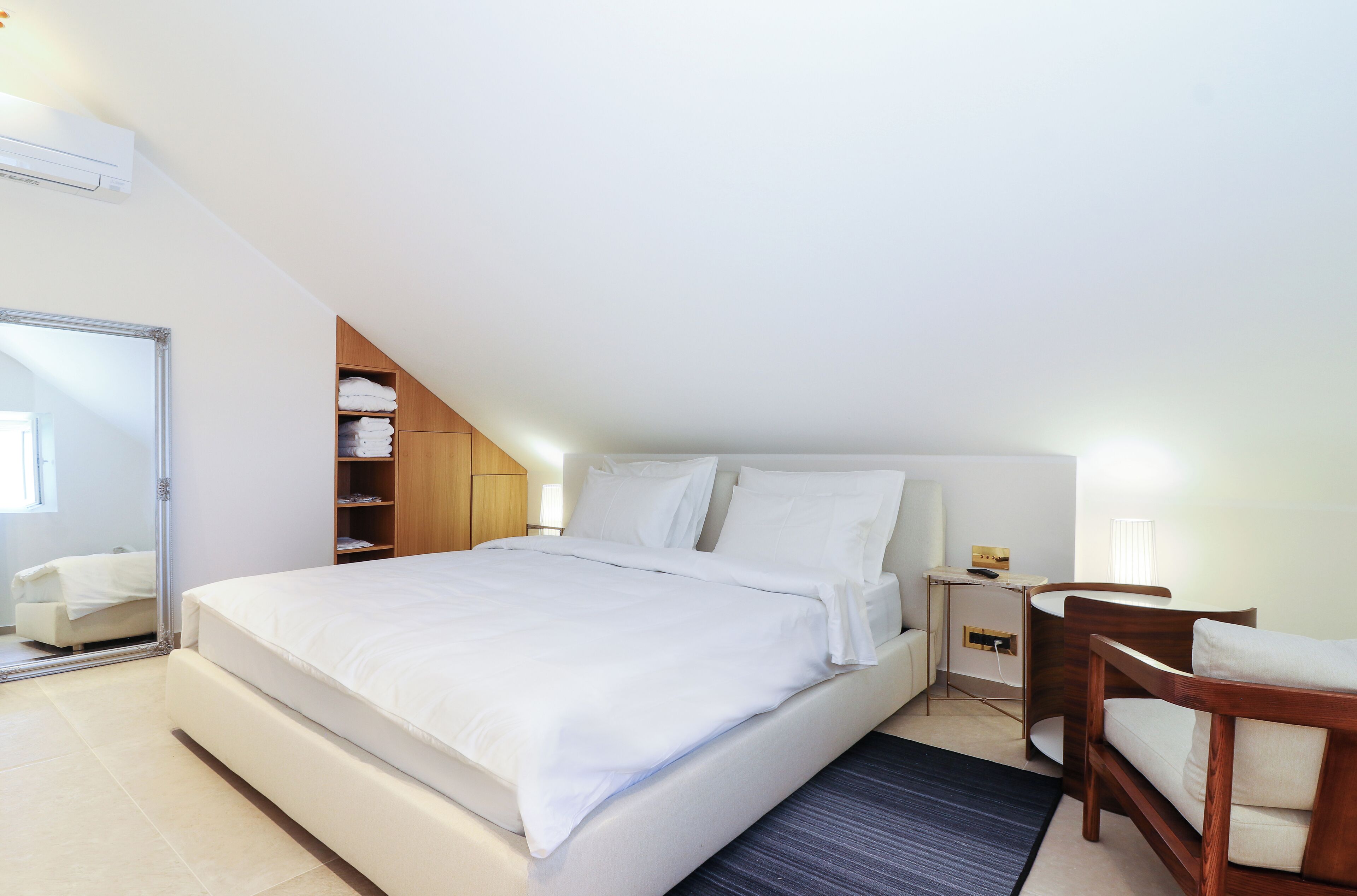 Une chambre à coucher moderne avec un grand lit, une tête de lit en bois, une table de chevet et une chaise.