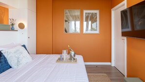 A bedroom with a bed, a bedside table with a vase and candles, a tray with champagne, and a TV on the wall. - Playful Bright 1BR Near The Faculty of Law (Bucharest)