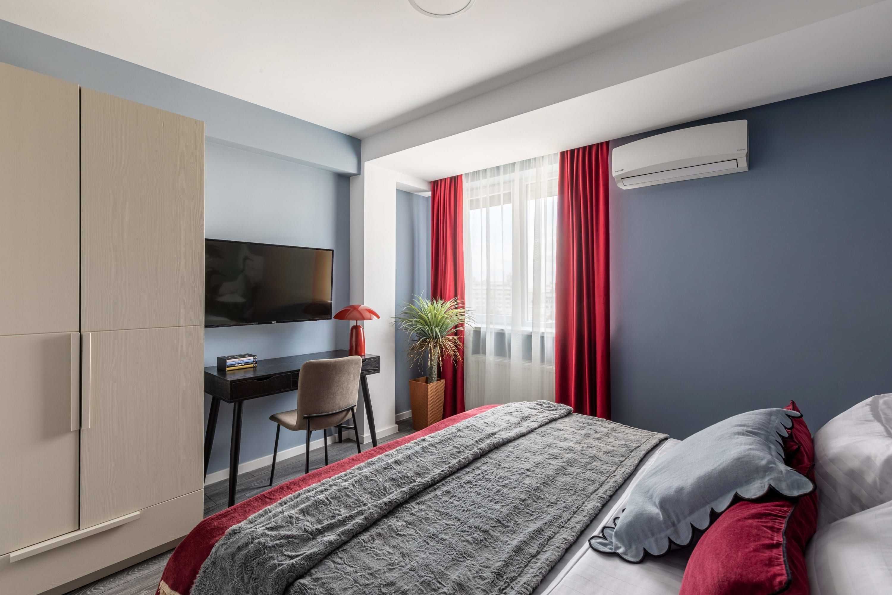 Ein Schlafzimmer mit Bett, Schreibtisch, Stuhl, Fernseher und einer Zimmerpflanze.