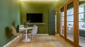 Un comedor con una mesa redonda y cuatro sillas, un televisor de pantalla plana en la pared y un puerta corrediza de vidrio que da a un balcón.